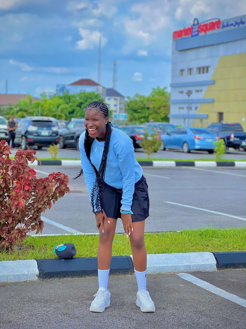 Divine outdoors in the same blue sweatshirt, white sneakers and crew socks, laughing with her hands on her knees.
